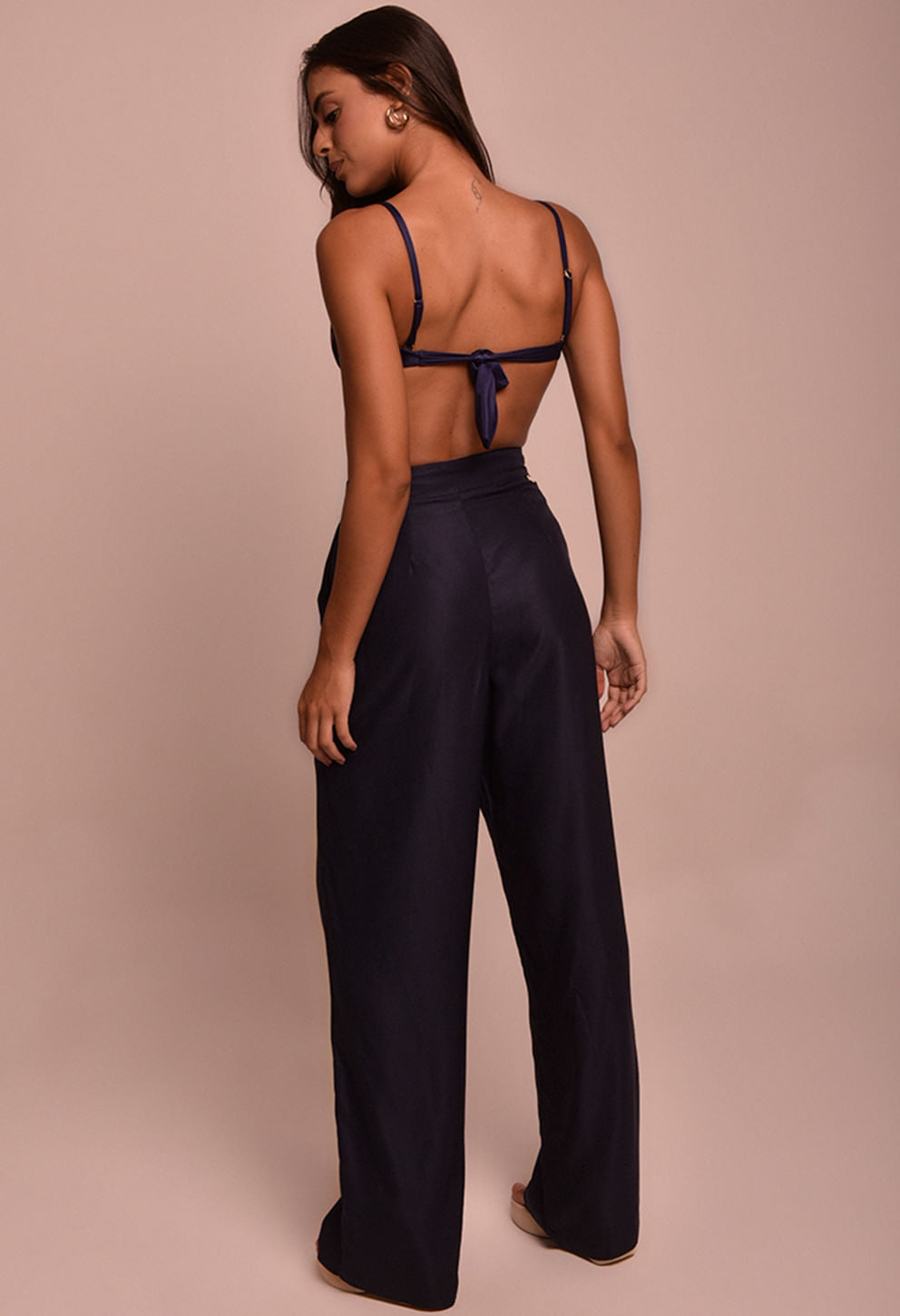 Calça pantalona preta feminina vista de costas com top azul marinho amarrado e alças finas.