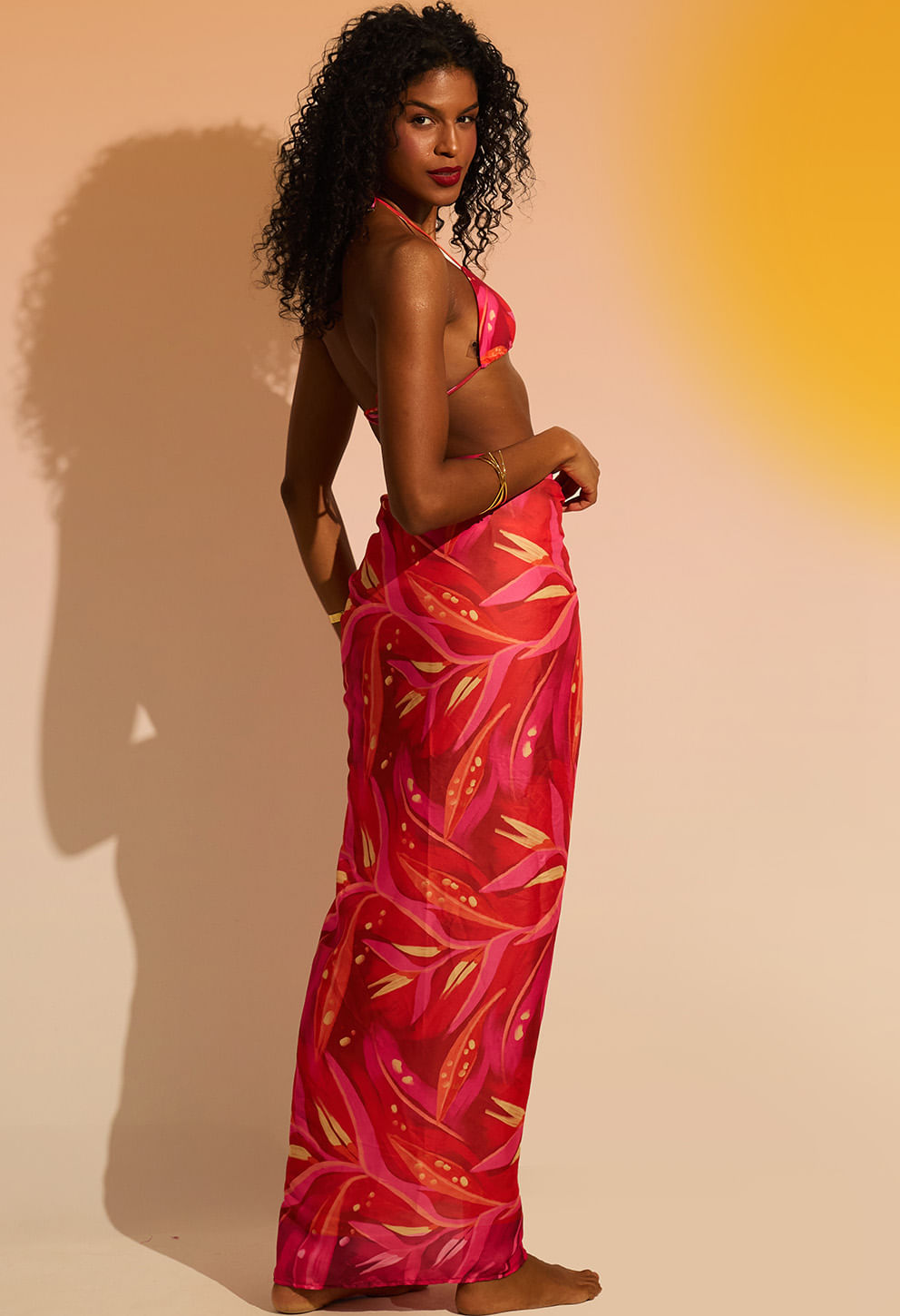 Mulher usando pareô rosa de verão com estampa floral em tons de vermelho e rosa, fundo claro degradê