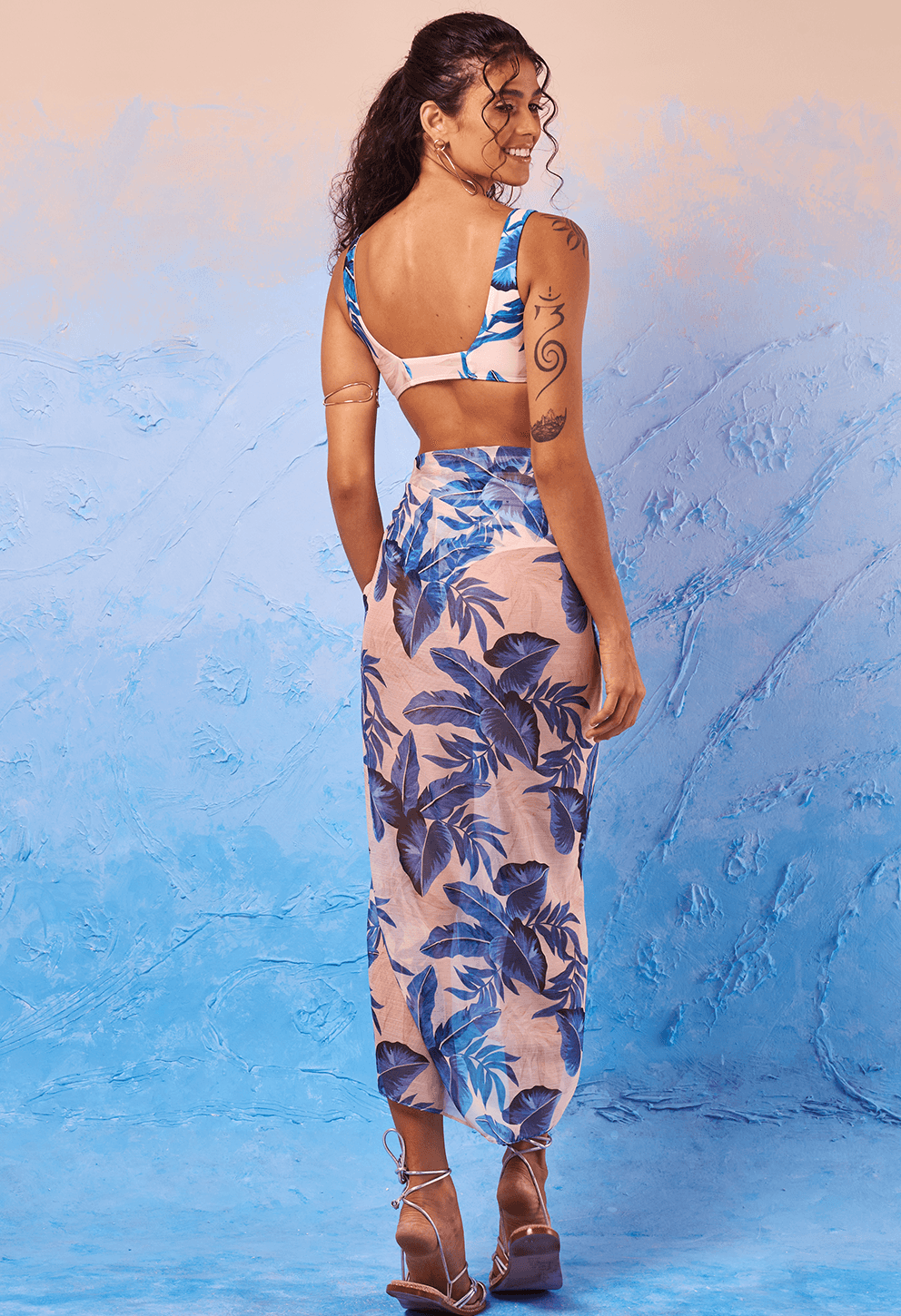 Modelo vista de costas usando top e pareô estampados Beach Terra Azul folhas azuis, fundo azul texturizado