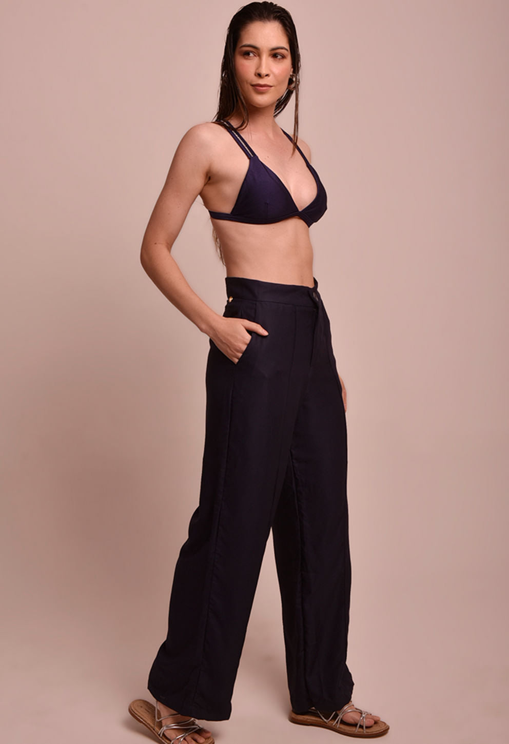 Calça pantalona marinho vista lateral com top de biquíni azul marinho usado por modelo, fundo bege.