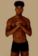 Homem usando sunga short adulto preta em fundo bege, vista frontal.