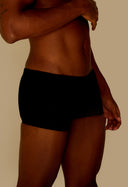 Vista lateral de homem usando sunga short adulto preta com fundo bege.