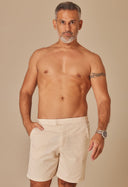 Homem usando bermuda alfaiataria bege clara, modelo frontal, fundo bege neutro