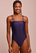 Body feminino azul marinho Yasmim com medalhas náuticas douradas nas alças duplas, modelo sorridente em fundo bege.