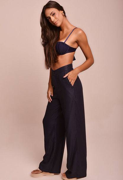 Calça pantalona preta feminina com cintura alta, bolsos e botão, combinada com top azul marinho com alças.