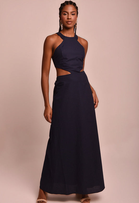 Vestido Martina Náutica azul marinho com recortes laterais e amarração nas costas, modelo usando vestido longo com fundo neutro.