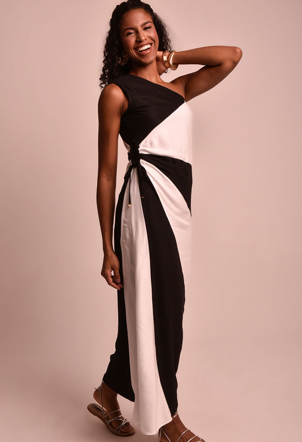 Modelo sorridente usando vestido longo bicolor preto e branco com amarração lateral, ombro só.