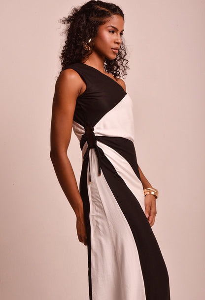 Vestido longo bicolor preto e branco com amarração lateral, vista lateral com acessórios dourados.
