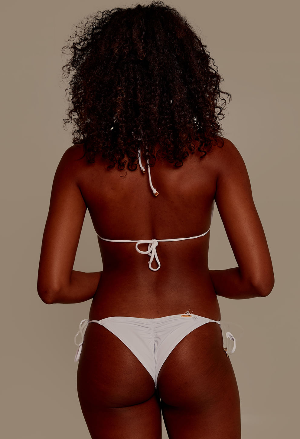 Mulher negra de costas usando biquíni branco com calcinha levanta bumbum, vista traseira.