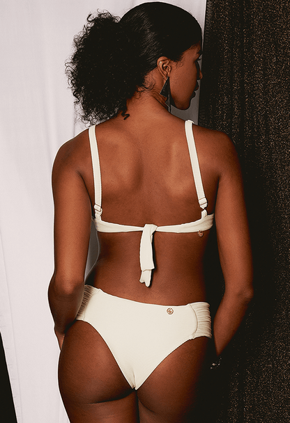 Calcinha Borboleta Lateral Larga Pé Na Areia branca creme em modelo feminina vista traseira.
