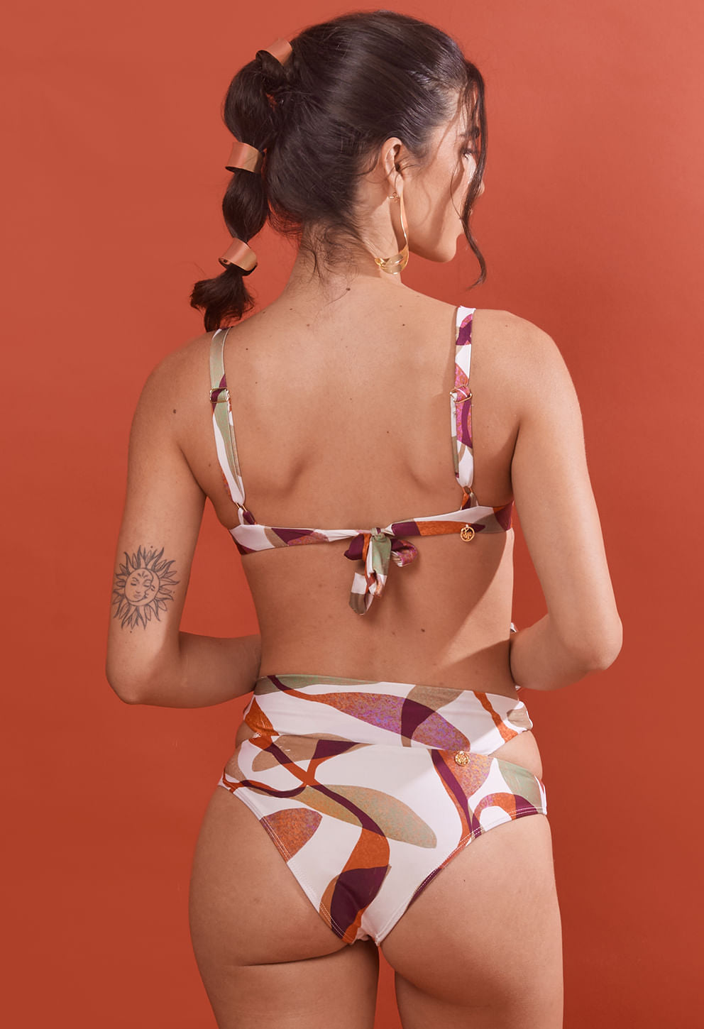 Biquíni calcinha Mary Cajueiro estampada com recortes laterais em fundo laranja, vista traseira