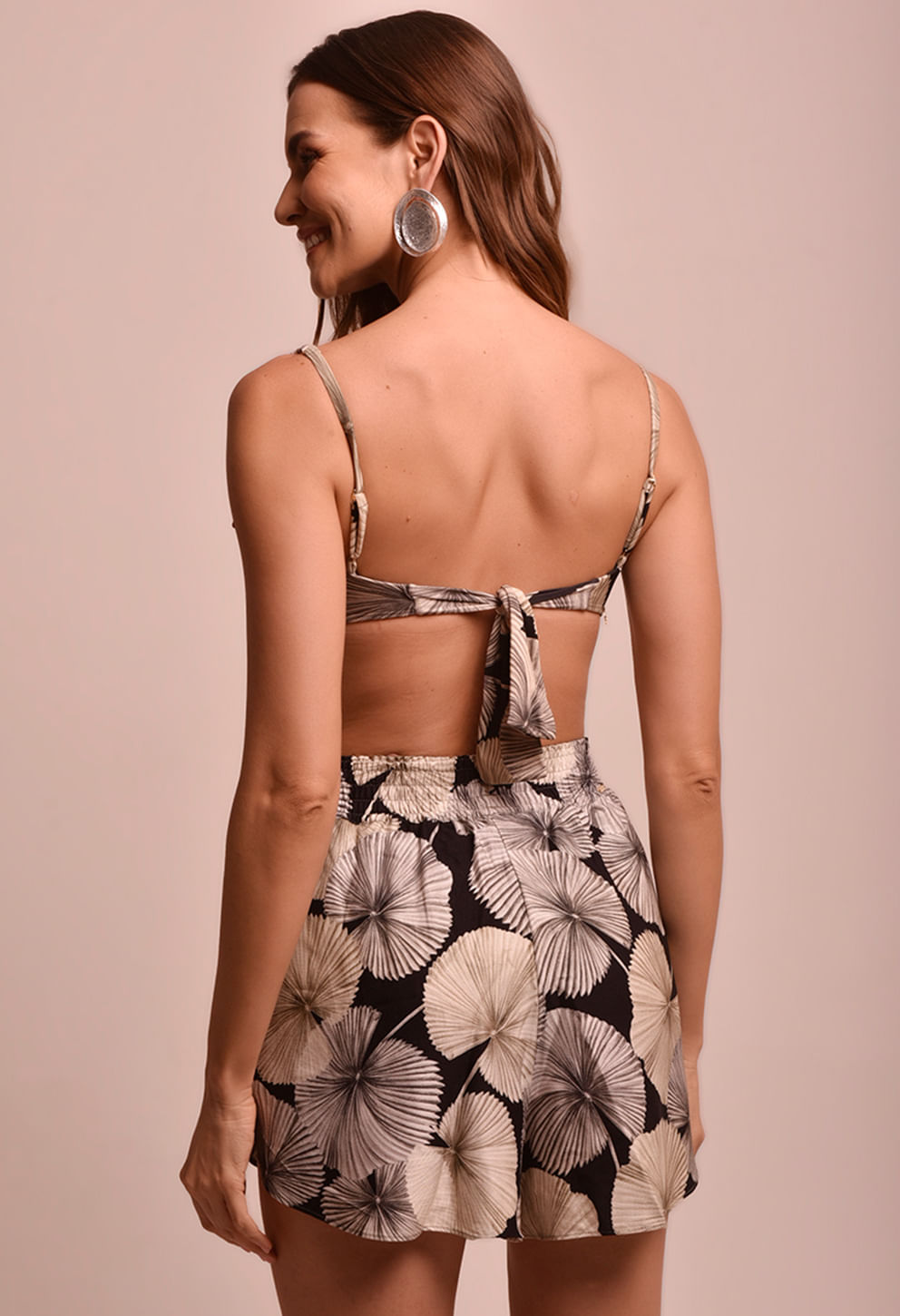 Short Malu Sublime feminino com estampa de folhas em tons de bege e preto, visto de costas, cós elástico, combinado com top tomara que caia, fundo neutro.