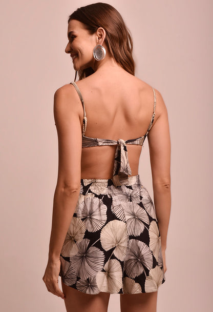 Short Malu Sublime feminino com estampa de folhas em tons de bege e preto, visto de costas, cós elástico, combinado com top tomara que caia, fundo neutro.