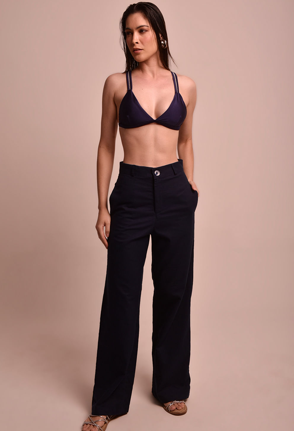 Mulher usando calça pantalona Malu Náutica azul marinho com top de biquíni azul, fundo neutro.