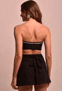 Modelo vista de costas usando saia mini transpassada preta Saia Mini Transpassada Luar com nó na parte de trás e top faixa preto.