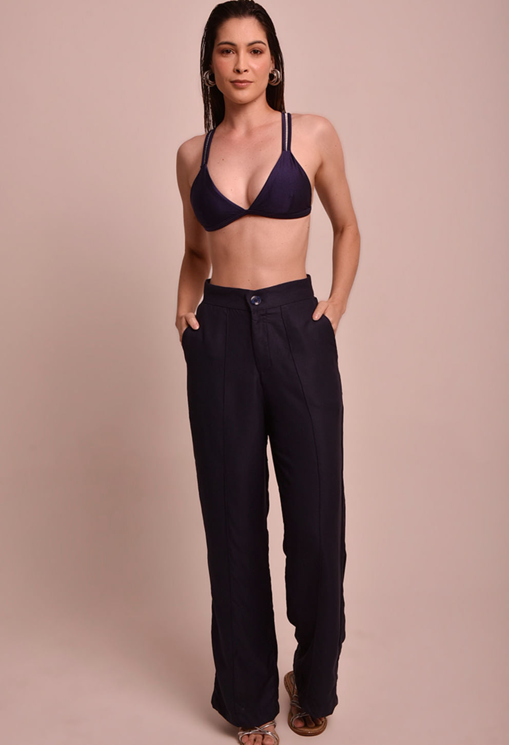 Calça pantalona marinho com cintura alta e bolsos laterais, usada com top de biquíni azul marinho, modelo frontal.
