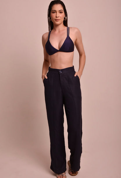 Calça pantalona marinho com cintura alta e bolsos laterais, usada com top de biquíni azul marinho, modelo frontal.