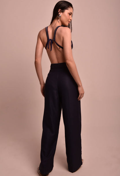 Calça pantalona marinho de cintura alta vista por trás, usada com top de biquíni azul marinho, modelo de costas.