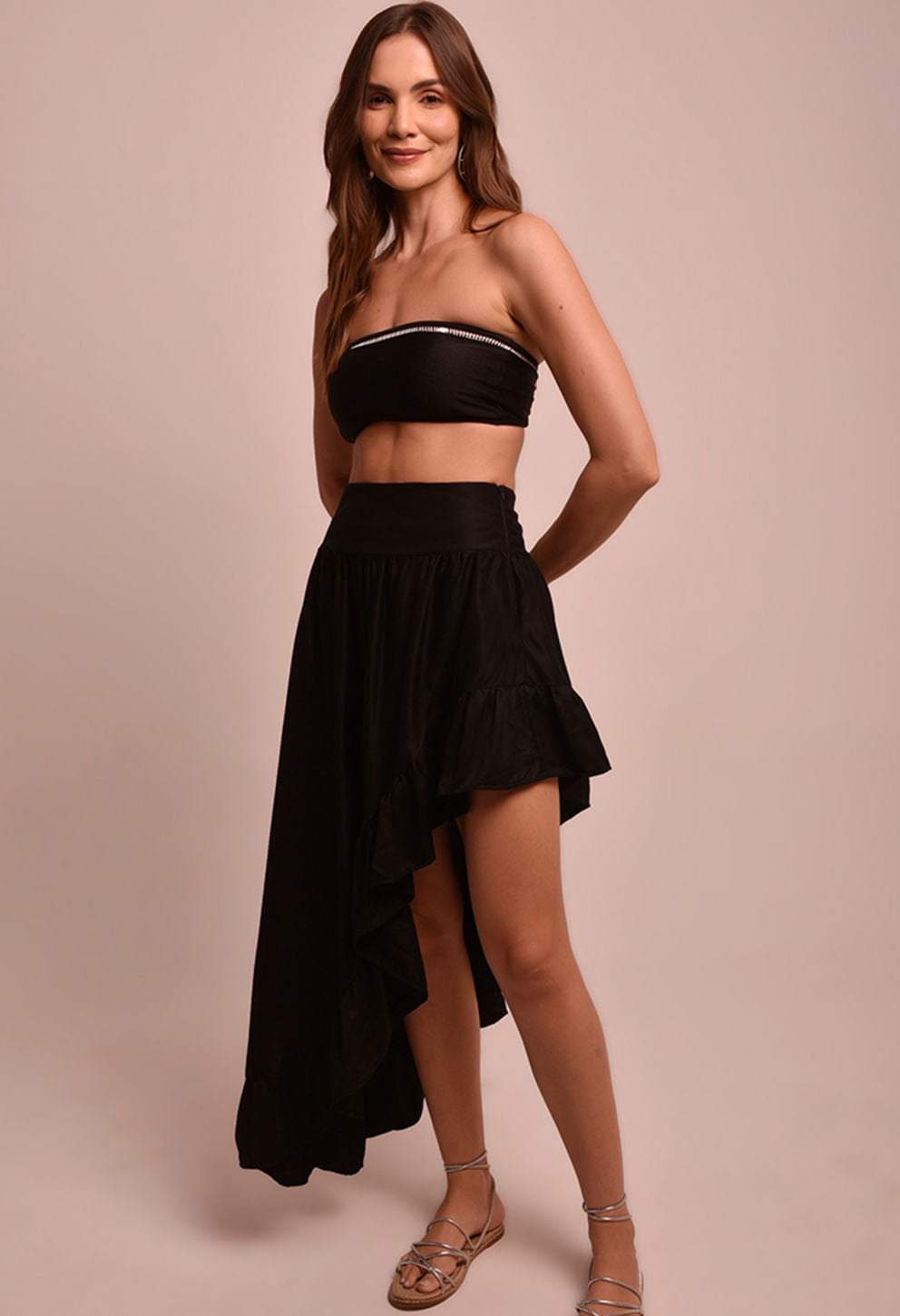 Modelo usando Saia Martha Luar preta assimétrica de babados e top faixa preto em fundo bege.