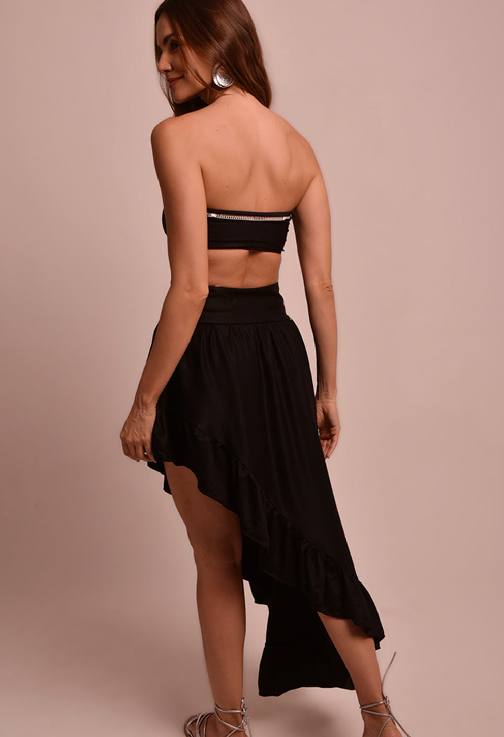 Perfil de modelo com Saia Martha Luar preta assimétrica de babados e top faixa preto, fundo bege.