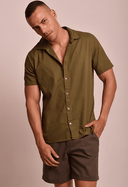 Camisa de linho slim manga curta verde army masculina com bermuda marrom, modelo masculino posando em fundo bege claro.