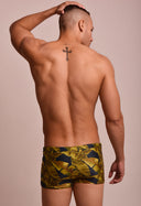Vista traseira de modelo masculino vestindo sunga short adulto com estampa de folhas amarelas e verdes sobre fundo preto.