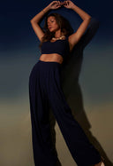 Calça pantalona básica marinho com top cropped combinando em modelo feminino, fundo degradê azul e bege.